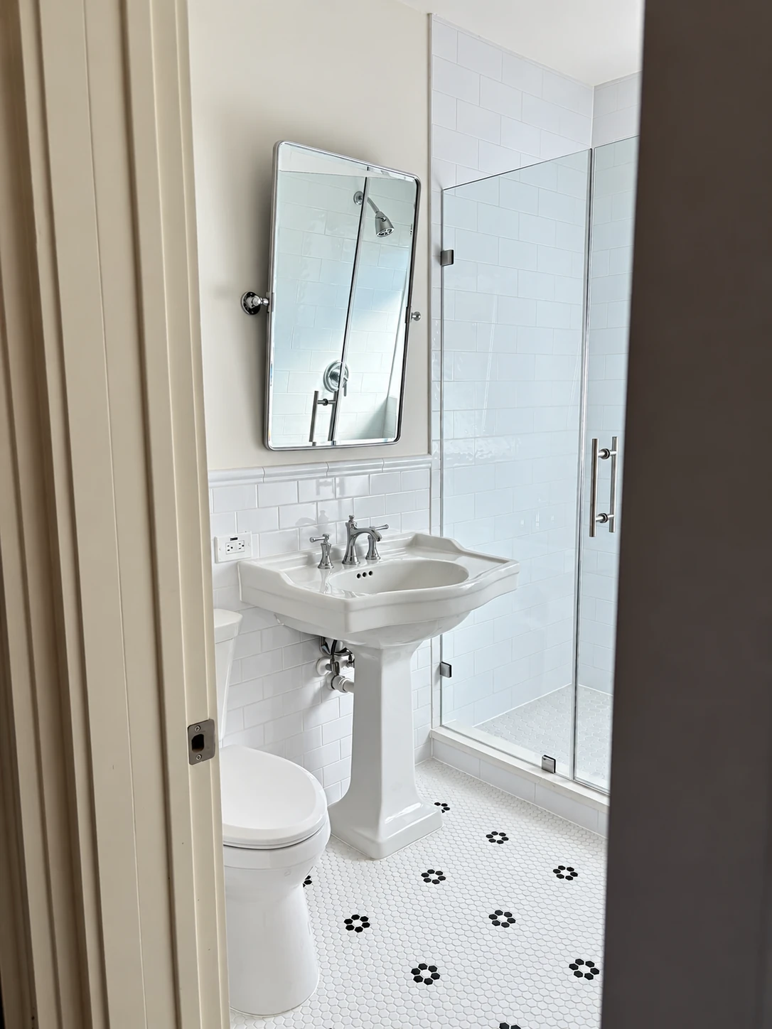 White tile bathroom with pedestal sink, glass shower, and patterned floor