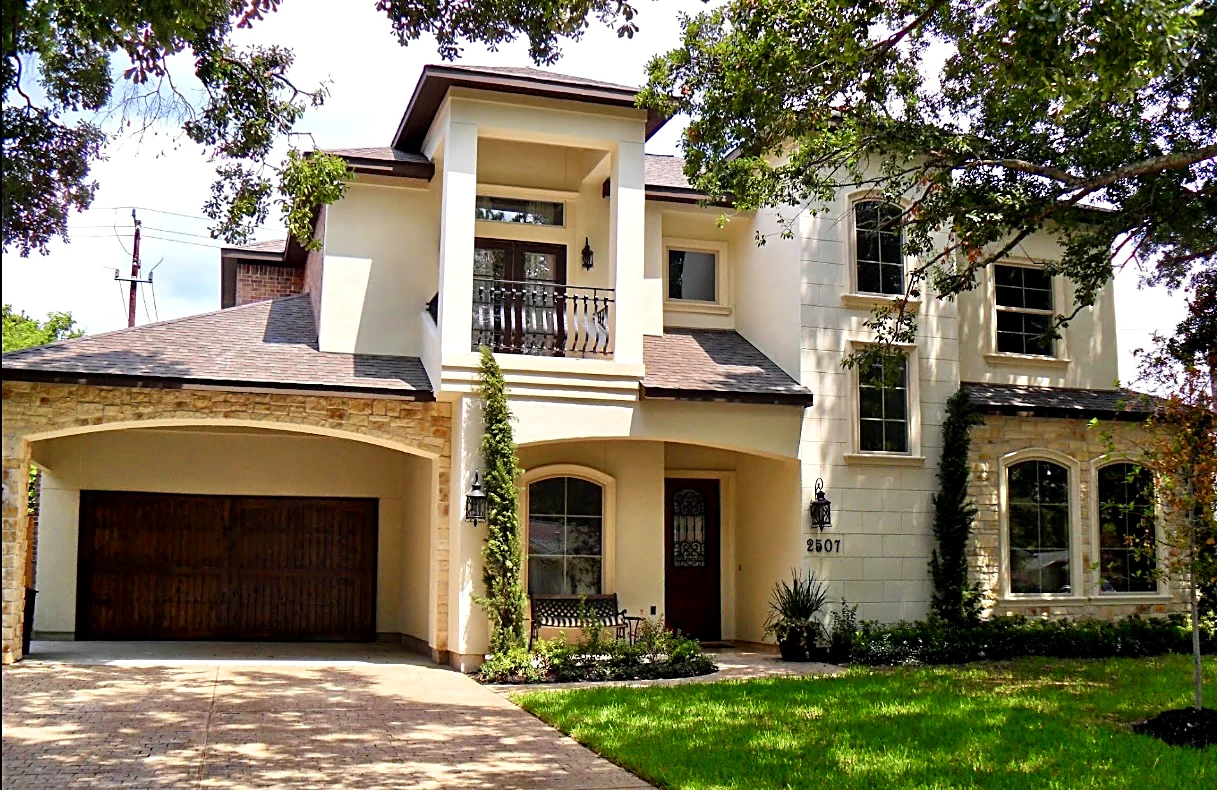 Custom home exterior — Two-story stucco and stone home with arched windows and a wood garage door.