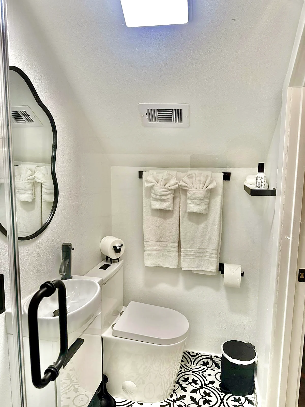 Garage apartment bathroom — Compact bath under the stairs with patterned tile floor and matte black fixtures.
