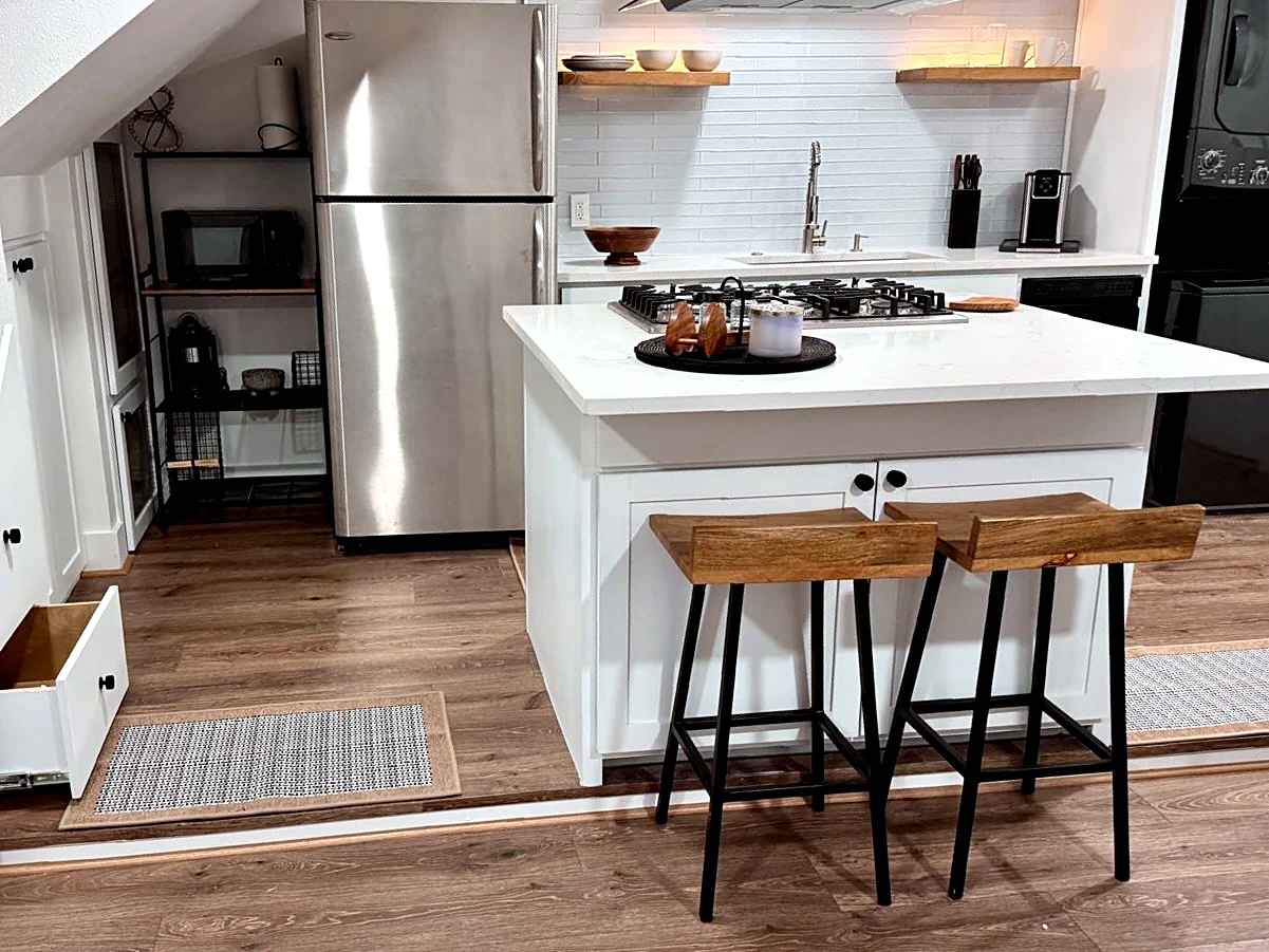 Garage apartment kitchen — White island with gas cooktop, quartz counters, and under-stair storage drawers.
