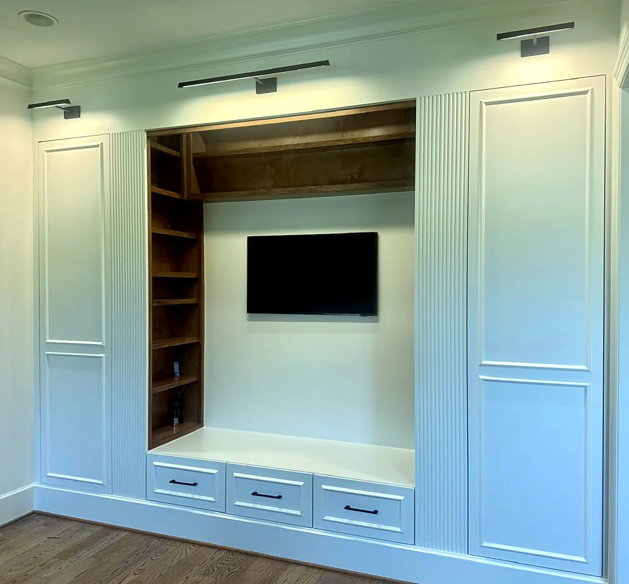 Media wall built-ins — White paneled cabinets with fluted trim, stained wood shelving, and accent lighting.